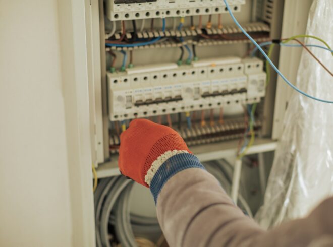 Electrician in safety gloves adjusting circuit breakers in an electrical panel, related to commercial electrical services and troubleshooting in Redondo Beach.